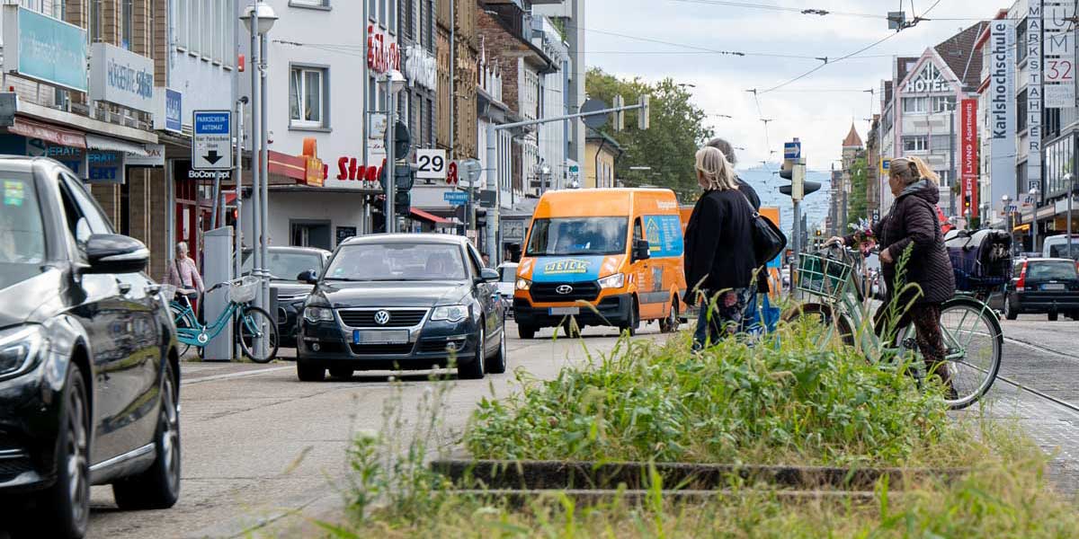 Straßenszene mit Autos, Fußgängerinnen und Radfahrerinnen.