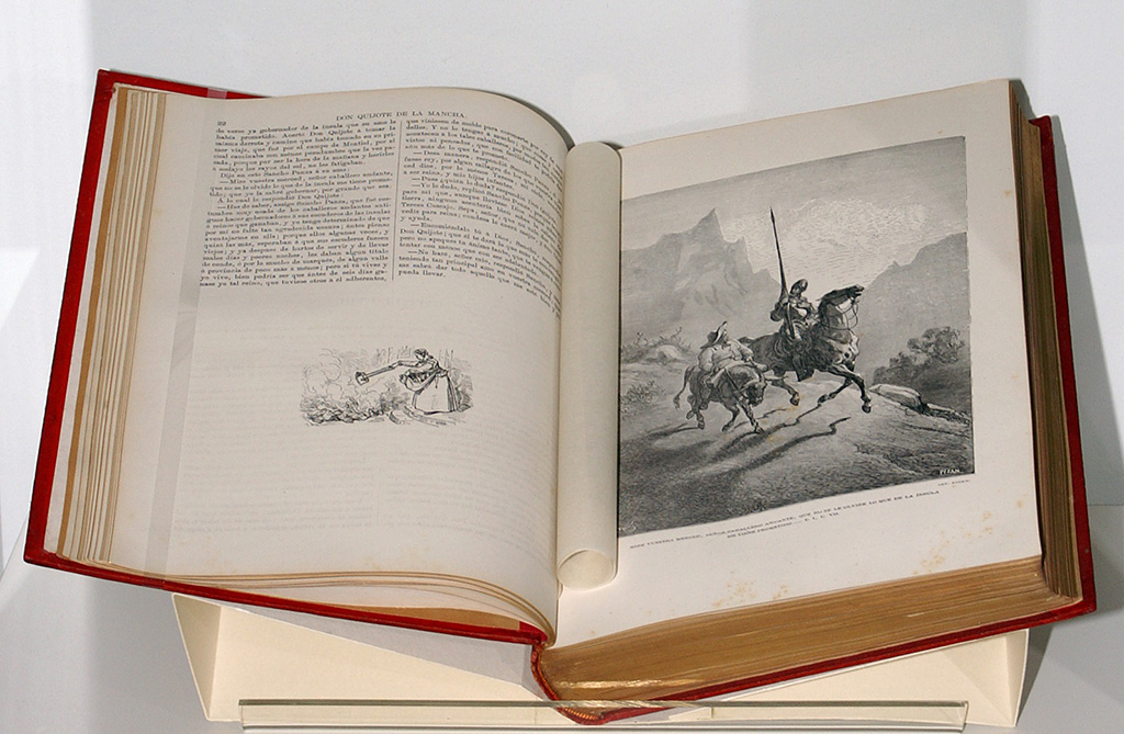 Zu sehen ist eine aufgeschlagene Ausgabe des Don Quichotte mit den Zeichnungen von Gustave Doré. Sie ist 1880 in Barcelona erschienen. Rechts ein ganzseitiger Stahlstich mit der Darstellung des Ritters Don Quichotte auf der Rosinante und des Sancho Panza auf seinem Esel.