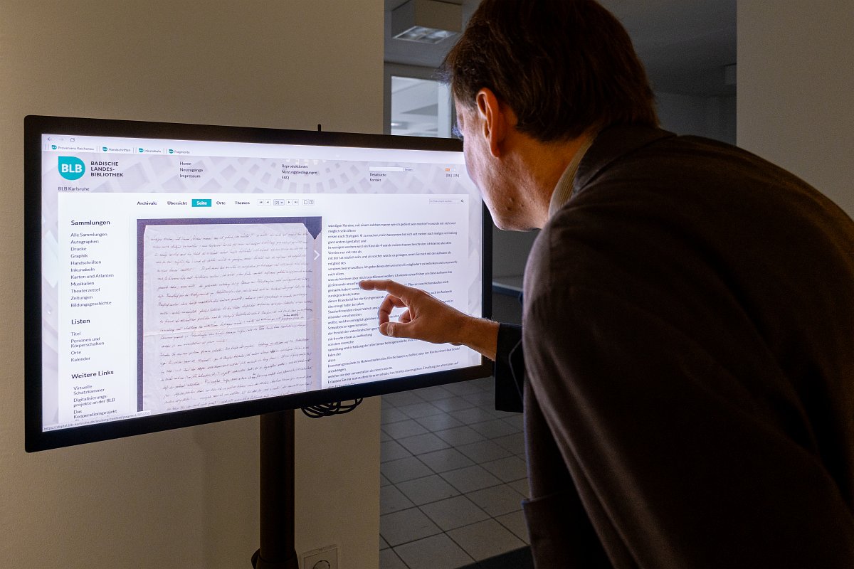 Blick in den Ausstellungsraum: Zu sehen ist eine Person, die einen Monitor bedient. Gezeigt werden die Digitalen Sammlungen mit den Neuerwerbungen.