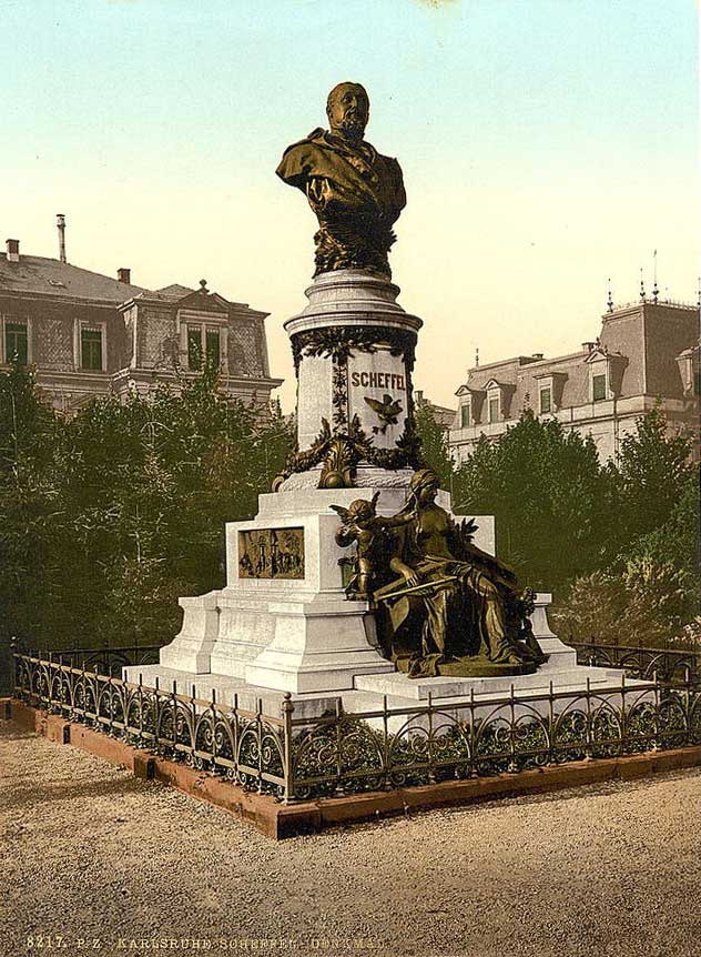 Auf dem Bild wird das Scheffeldenkmal auf dem Scheffelplatz in Karlsruhe dargestellt. Das Denkmal besteht aus einer bronzenen Büste, die Joseph Victor von Scheffel abbildet, welche auf einer Säule auf einem Podest steht. Am Sockel wurde eine große Musenfigur, ebenfalls aus Bronze, platziert. Seitlich am Sockel ist ein Relief zu erkennen, sowie weitere Verzierungen. 